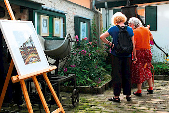 2 Frauen im Hof eines Ateliers, im Vordergrund ein Gemälde auf einer Staffelei