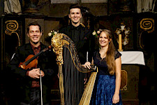 Ein Violinist, ein Mann in schwarzem Frack und eine Frau mit Harfe posieren