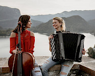 Zwei junge Musikerinnen sitzen auf einer Mauer hoch über einem See