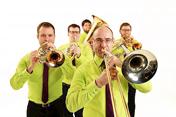 Embrassment Blechbläserqiuntett Foto. Die fünf Musiker stehen vor einem weißen Hintergrund. Sie tragen neongrüne Hemden und schwarze Krawatten. Ihre Blechbläser haben sie bereit zum losspielen in ihren Händen und am Mund angesetzt.