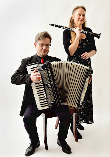Miroslaw Tybora sitz mit seinem Akkordeon auf einen Stuhl. Susanne Ehrhardt steht schräg hinter ihm mit ihrer Klarinette.