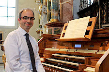 Ein Mann mit Brille: er sitzt vor dem Orgel und lächelt