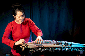 Eine Asiatin zupft die Saiten an einem Instrument