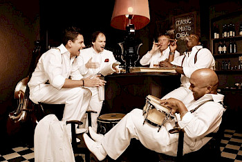 Weiß gekleidete Männer sitzen um einen Tisch und lachen