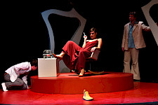 Eine Frau und zwei Männer auf einer Theaterbühne