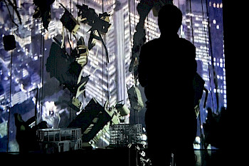 Ein Mann steht vor einem Hintergrund. Der Hintergrund skizziert eine moderne Stadt anhand von vielen Lichteffekten