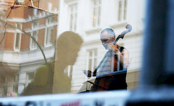 Ein Mann spielt Cello hinter dem Glass