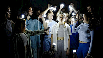 Ein Mädchen steht in der Mitte. Die andere Jugendliche stehen herum mit Lampen in den Händen.