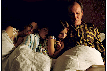 Eine Familie, Papa, Mama, Sohn und Tochter, liegen gemeinsam auf einem Bett