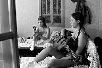 2 Mädchen, 1 spielt Guitarre, 1 schaut sich in dem Spiegel