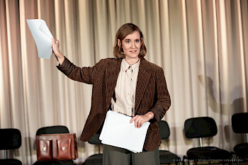 Eine Frau steht auf der Bühne mit Papier in den Händen