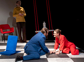 Eine Frau in rot und ein Mann in blau sitzen auf einem Schachbrett