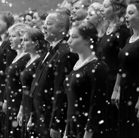 Viele SängerInnen eines Chors singen, im Vordergrund rieselt Schnee