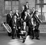 11 Männer in Anzügen und Blechbläsermusikinstrumenten