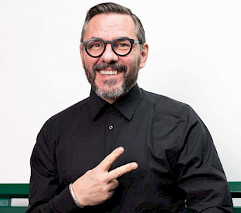 Ein Mann mit Brillen und schwarzem Anzug, er zeigt «Peace»-Zeichen