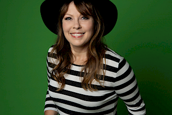 Eine Frau mit süßem Lächeln und einem Hut vor dem grünen Hintergrund