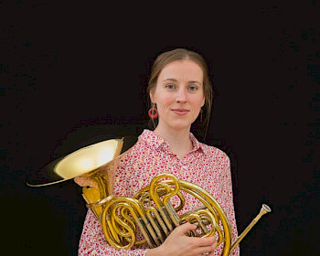 Junge Frau mit blauem Hemd hält das Blasinstrument Horn