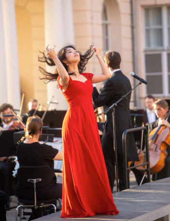 Eine hübsche Sängerin spielt mit ihren Haaren auf der Bühne. Sie trägt ein rotes Kleid