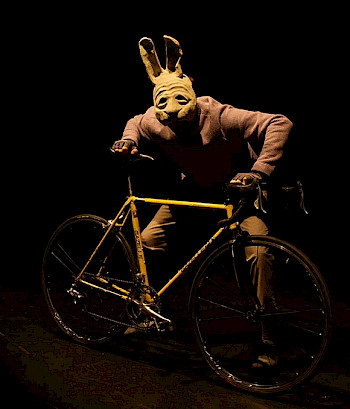 Ein Mann mit Hasenmaske, er hält einen Fahrrad