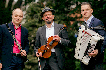 3 Männer mit Musikinstrumenten in Händen: Klarinette, Akkordeon, Violine