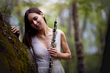 Eine Frau steht neben einem Baum und hält eine Oboe