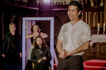 Ein junger Mann in weißem Hemd steht vor drei weiteren Schauspielern auf einer Bühne