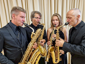 3 Saxophonisten und eine Saxophinistin stehen im Kreis und musizieren