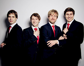 Vier junge Männer mit Anzügen und roten Krawatten stehen nebeneinander