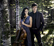 Ein Mann im Anzug steht hinter einer langhaarigen Frau mit Cello in einem Birkenwald