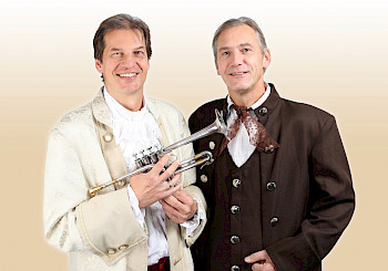 Zwei Männer mit Trachtenjacken, einer hält eine Trompete.