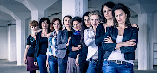 9 Frauen stehen aufgereiht hintereinander in einer leeren Fabrikhalle