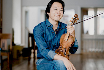 Lächelnder Asiate in Jeanskleidung mit Violine in der Hand