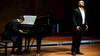 Ein Mann singt, begleitet von einem Pianisten, auf einer Bühne