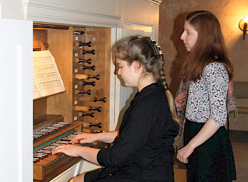 Eine junge Frau spielt an einer Orgel. neben ihr steht eine weitere junge Frau