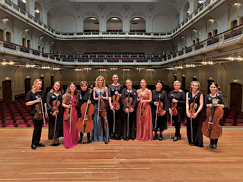 Orchestermitglieder stehen mit ihren Instrumenten auf einer Opernbühne
