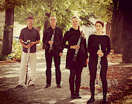 4 Musiker mit Klarinetten stehen unter Bäumen