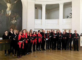 Chor mit Einheitskleidung schwarz-rot und Notenbüchern in den Händen vor einem Jesusbild in einer Kirche