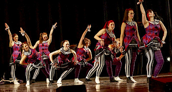 Frauen in karnevalsartigen Kostümen tanzen auf der Bühne
