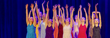 Eine Gruppe Mädchen reckt auf einer Bühne alle Hände in die Höhe