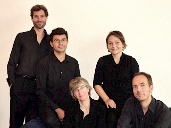 5 Männer und Frauen posieren vor neutralem Hintergrund. Alle tragen schwarze Kleidung