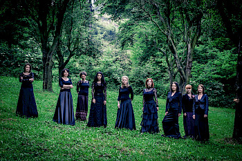 9 Frauen tragen schwarzen Klamotten. Sie posieren im Wald