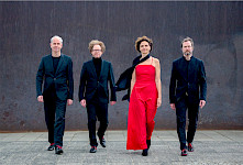 4 Musiker laufen nach vor zusammen. Die Frau trägt eine roten Kleid