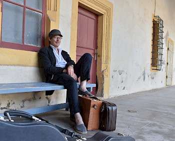Mann mit Basecap und Koffern auf einer Bank sitzend