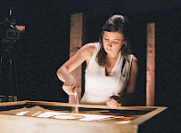 Eine Frau streut Sand auf eine beleuchtete Tischplatte