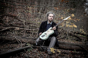 Tobias Hoffmann sitzt im Wald mit seinem Gitarren
