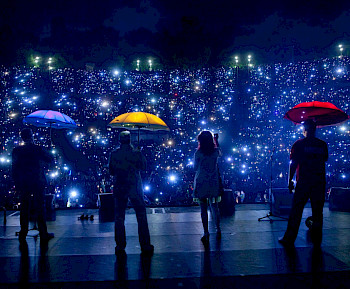 4 Leute mit bunten Schirmen stehen in blauer Licht