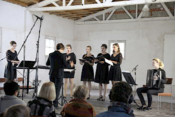 7 Musikerinnen stehen auf der Bühne in der ehemaligen Textilfabrik der Gedenkstätte Ravensbrück