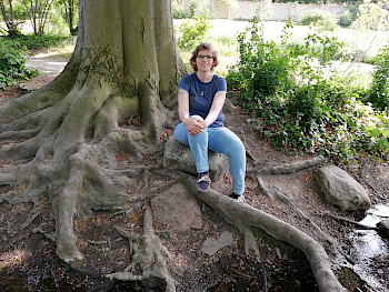 1 Frau sitzt vor einem Baum