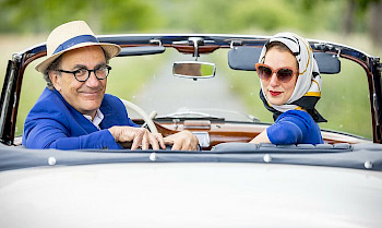 1 eleganter Paar sitzt auf einem Roadster. Sie schauen rück und lächelt