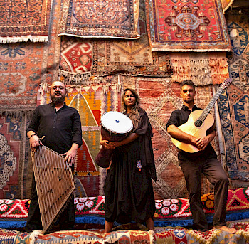 1 Frau und 2 Männer mit orientalen Musikinstrumenten, hinter ihnen sind verschiedene Teppiche